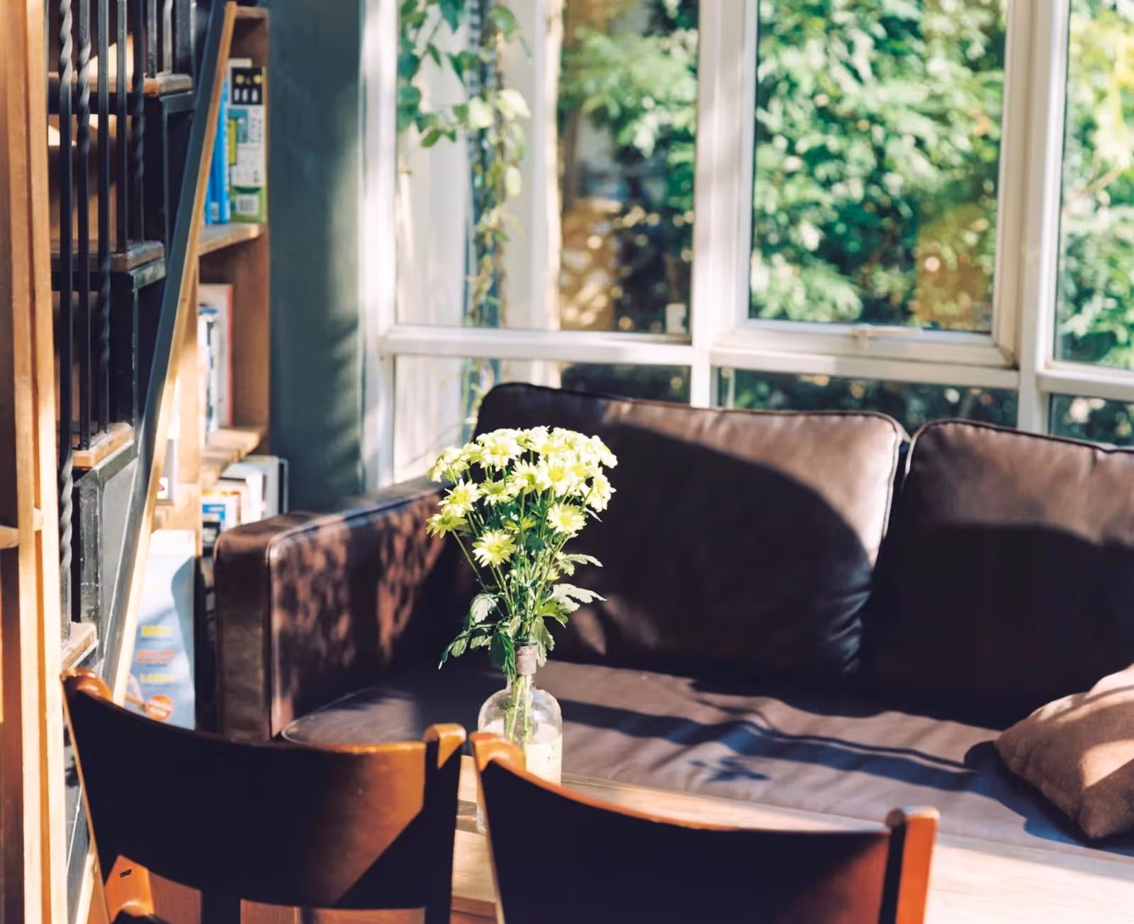 A warm, sunlit living room with a bookshelf and fresh flowers on the table