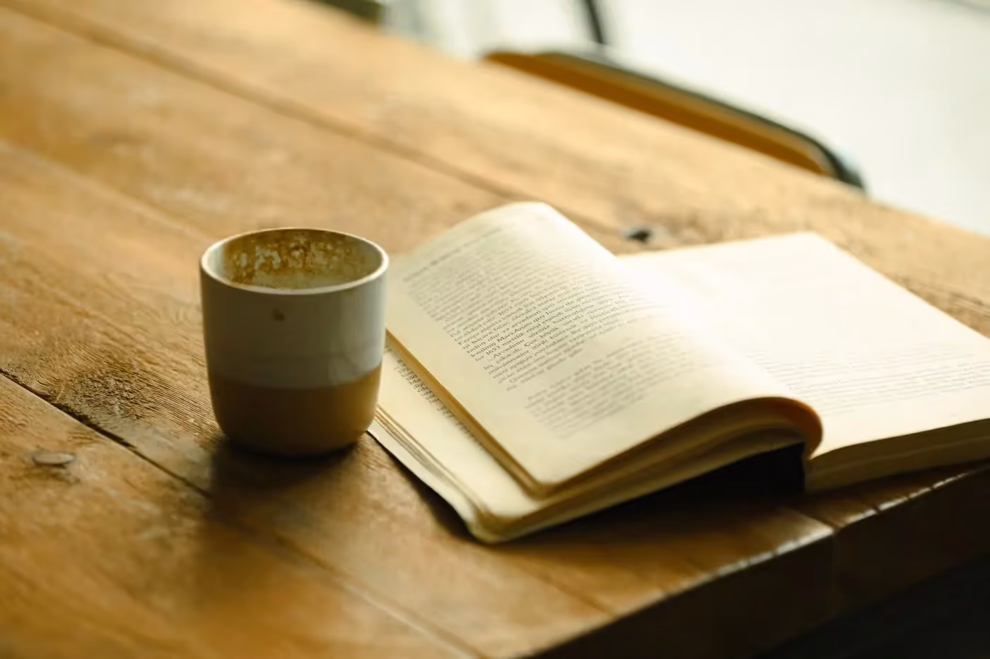 A warm wooden table with a mug and an open book in soft morning light